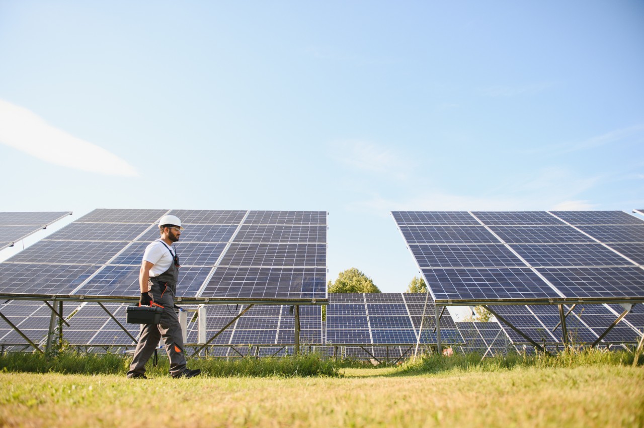 Indian man in uniform on solar farm. Competent energy engineer controlling work of photovoltaic cells