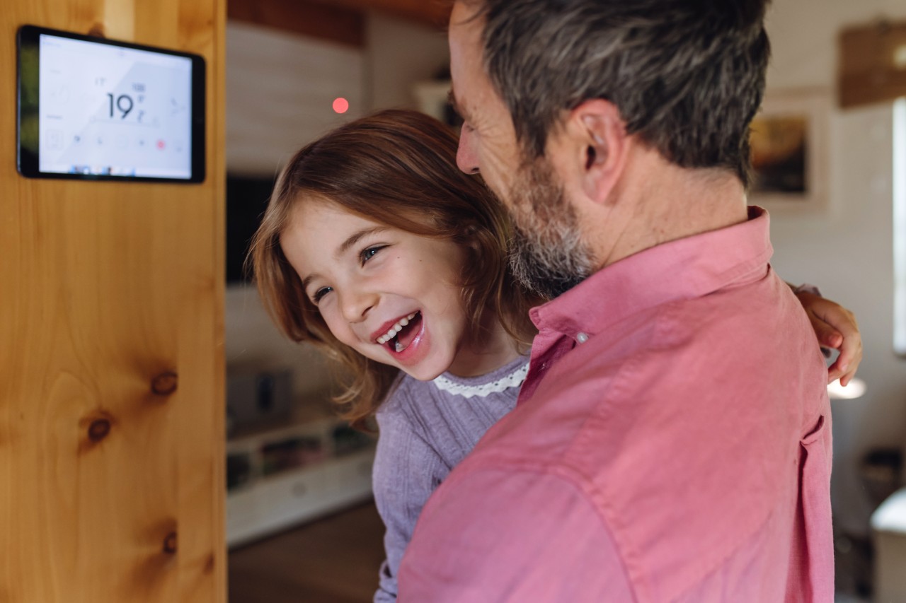 Father looking at smart thermostat, adjusting, lowering heating temperature at home. Concept of sustainable, efficient, and smart technology in home heating and thermostats.